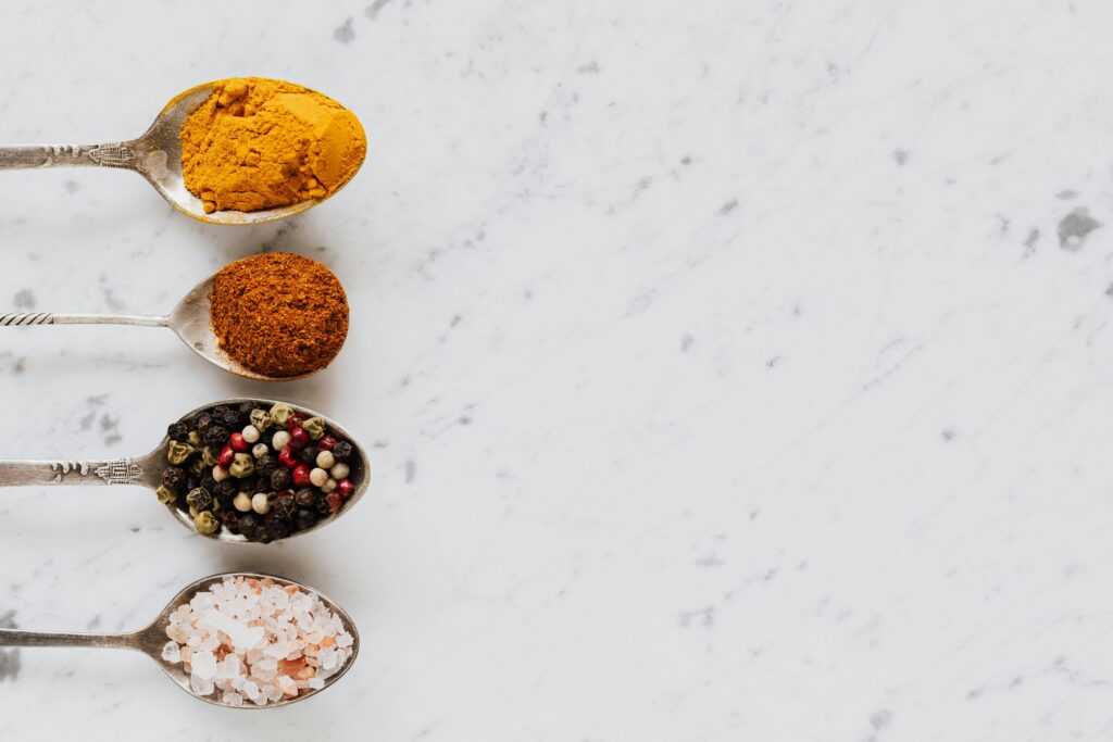 An assortment of colorful spices on spoons laid on a marble surface.